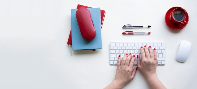 Woman hands on laptop keyboard with wireless mouse, cup of coffee, red notebook on white table. Office desktop with copy space.