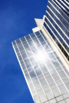 Geometric glass windows on a skyscraper with sun reflecting a lens flare against a blue sky background from below. Exterior architectural details of a modern and tall high rise building in the city