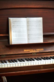 Old vintage piano with musical notes at a classical music festival. An antique wooden keyboard with a composition book ready for a melody to be created in an art gallery. A classic musical instrument