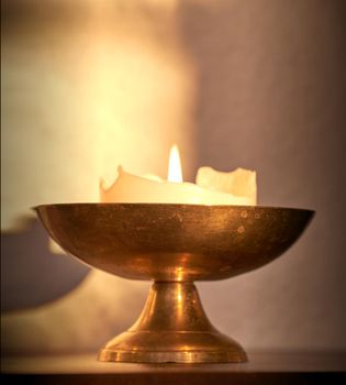 Lit candle on a table at home for warmth and brightness. Beautiful house decoration used for aroma, good scent and to bring light to a room. Candles represent light, illumination, and purification