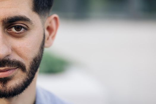 Half face portrait of young man with beard. Half face of upset bearded caucasian young man looking straight to camera while standing outdoors in empty town
