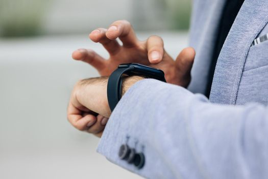 Closeup shot of male's hand uses of wearable smart watch at outdoor. Smartwatch on a business man's hand outdoor. Gorgeous businessman touching a smart watch. Smart watch