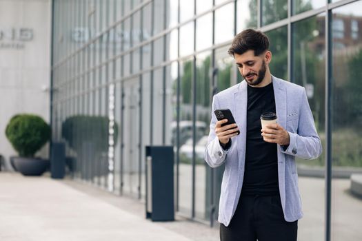 Gorgeous bearded businessman using mobile phone for texting during way to office in financial district, successful male proud ceo smiling during cellular messaging.