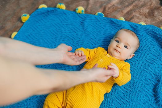 A small child 4-5 months old lies on a bed in yellow clothes. The child begins to hold his head. Baby clothes