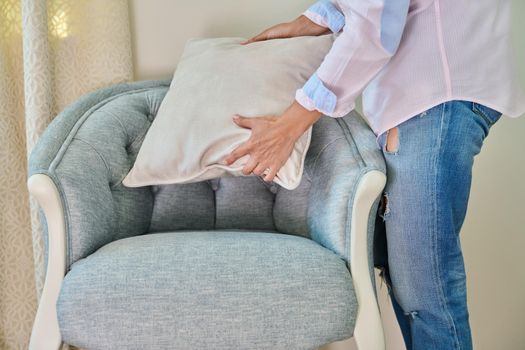 A woman decorating blue armchair with velvet beige cushion