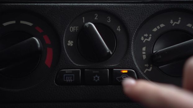 The woman turns on the fan and presses the button for the internal ventilation in the car. Automotive panel close-up.