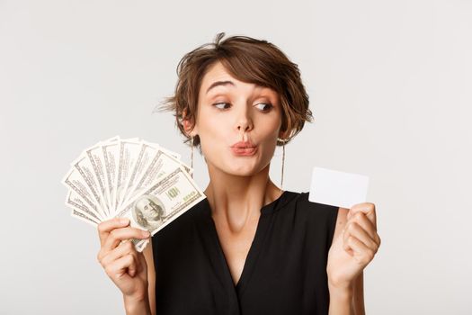 Young woman prefer credit card over money, standing over white background