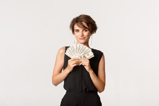 Sassy businesswoman showing money and smiling at camera, standing over white background