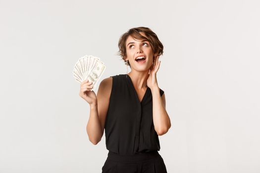 Gorgeous rich girl showing money and looking sassy, standing over white background