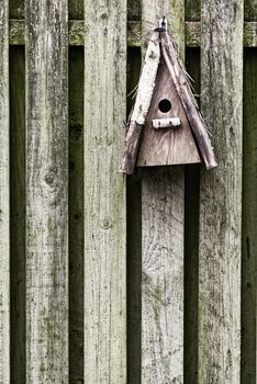 Old, wooden, and rustic bird feeder hanging on a fence in a backyard garden. Closeup of a vintage birdhouse on a wall outside. Built enclosures for birds in their natural environment and habitat
