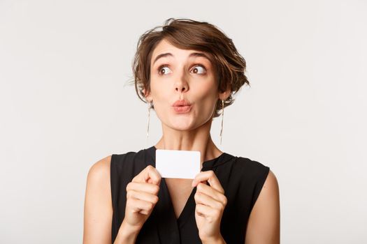 Image of curious girl looking left at product and showing credit card, standing over white background