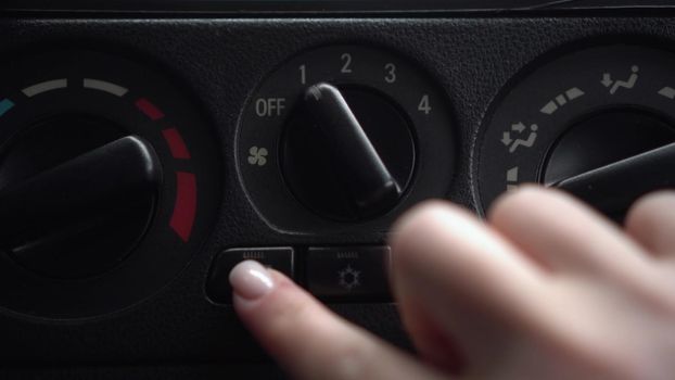 The woman turns on the fan and presses the window heating button in the car. Automotive panel close-up.