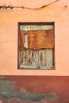 Abandoned and bordered window on an empty house from poverty and economic crisis in Santa Cruz, La Palma, Spain. Wooden boards covering and blocking an old village home with damp mold on the walls