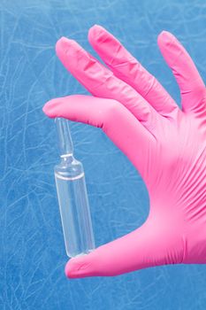 Hand of female doctor in pink glove with ampoule and medicine