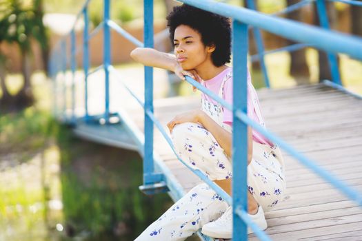Dreamy black woman sitting on footbridge