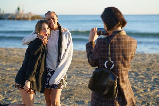 Faceless woman photographing positive diverse girlfriends near sea