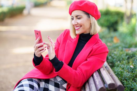 Cheerful woman browsing smartphone in park with red clothes.