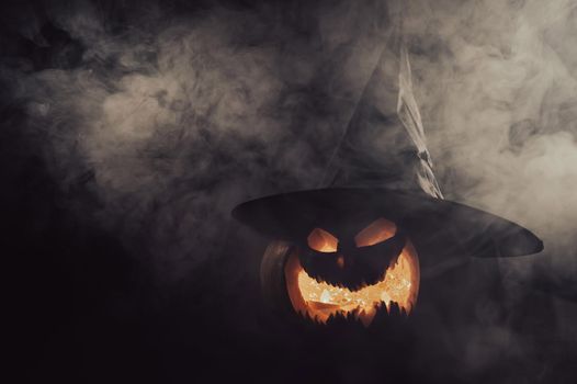 A creepy pumpkin with a carved grimace in the smoke. Jack o lantern in the dark.