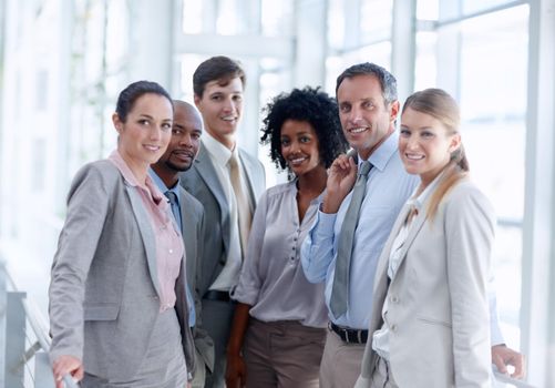 Close-knit business team. Diverse business team stand closely together as they look at you.