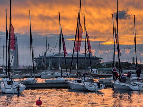 Russia, St. Petersburg, 12 July 2022: The yacht club with piers and sailing boats against the backdrop of the expressway and the football stadium Gazprom Arena at sunset, flags and masts