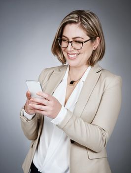 Instant access to business updates. Studio shot of a young businesswoman using a mobile phone against a gray background.