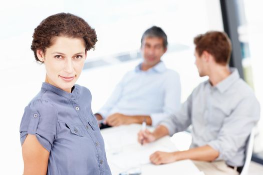 Boardroom positivity. Portrait of an attractive office worker with her coworkers seated behind her.