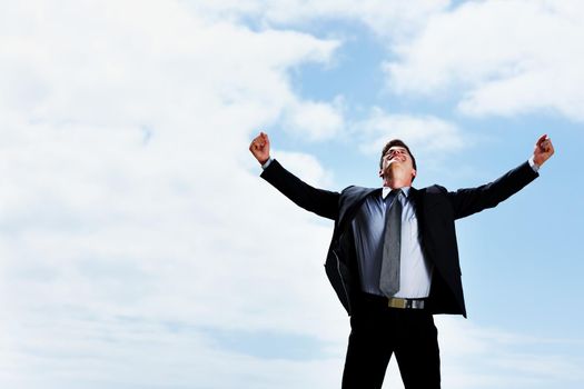 Happy business man with arms wide open against sky. Successful business man with arms wide open looking up against sky.