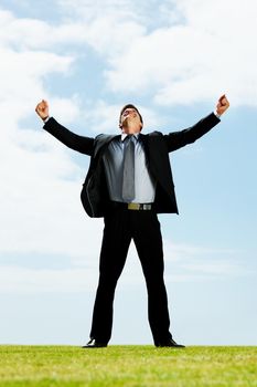 Celebration - Happy business man with his arms outstretched on a field. Full length portrait of a successful business man looking up with his arms outstretched on a field.