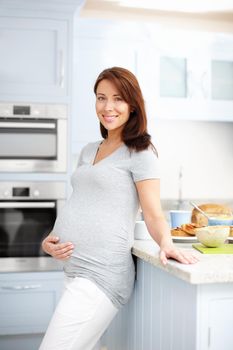 Catering for two. Portrait of a beautiful pregnant woman standing in the kitchen holding her stomach.