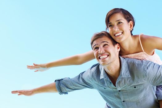 Couple enjoying outdoors. Portrait of young couple enjoying with arms outstretched against blue sky.