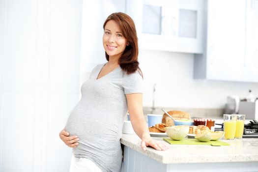 Keeping up with her lifestyle. Young expecting woman holding her tummy as she stands in her kitchen.
