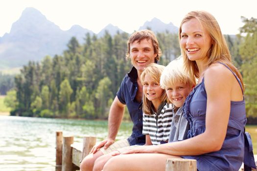 Enjoying quality family time outdoors. Cute young family sitting on the jetty near a lake and smiling.