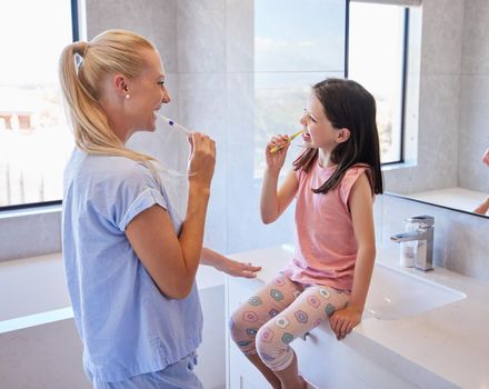Young caucasian mother and her little daughter brushing their teeth with toothbrushes in the morning.Teaching your children the basics of good oral hygiene