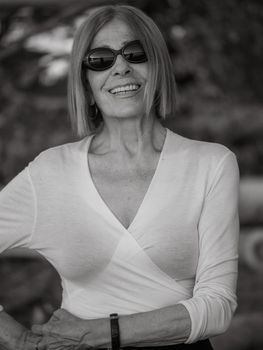 elegant caucasian senior woman wearing sunglasses sitting in a park at dusk