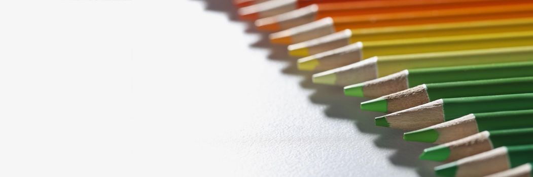 Colourful pencils set perfectly arranged in line on white surface