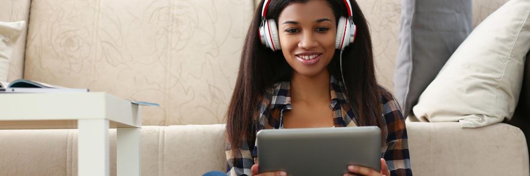 Latin young woman sit on carpet with tablet and watch show, lady in headset