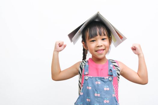 Back to school. Smiling little girl carrying a backpack holding books on her head looking at the camera on a white background with copy space. Girl glad ready to study.