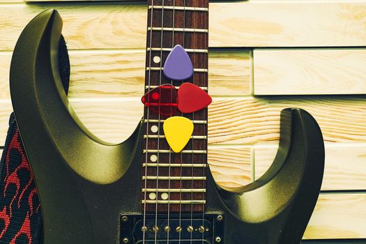 Black electric guitar with plectrums in strings on a wooden block background