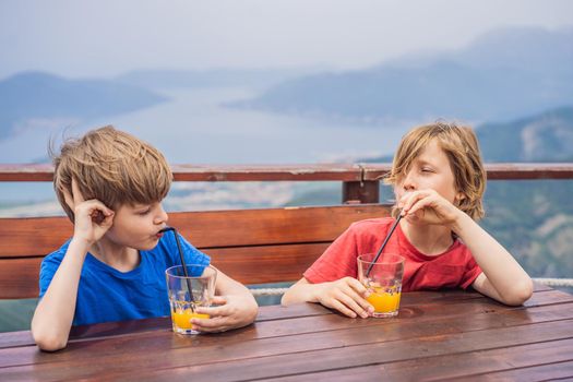 Two boys friend drink juice, enjoys the view of Kotor. Montenegro. Bay of Kotor, Gulf of Kotor, Boka Kotorska and walled old city. Travel to Montenegro concept. Fortifications of Kotor is on UNESCO World Heritage