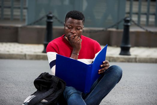 Handsome college man reading notes in notebook on campus.