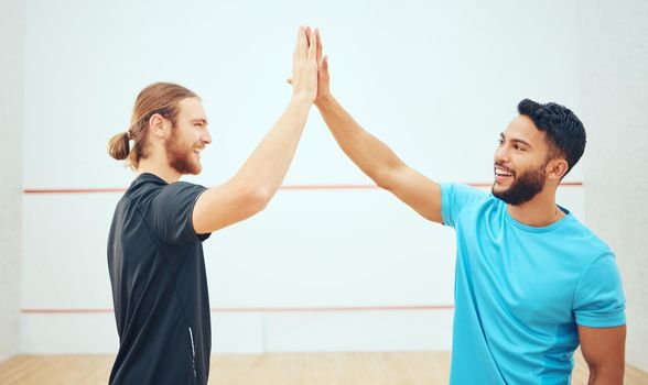Two athletic squash players giving high five before game on court. Team of fit active caucasian and mixed race male athletes using hand gesture before competing and training together in sports centre