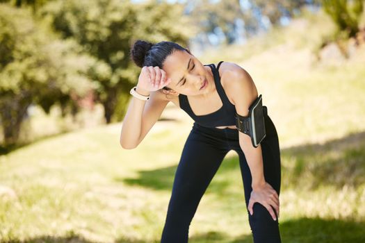 One active young mixed race woman taking a break from exercising outdoors. Hispanic athlete wiping sweat off forehead after a jog or run outside. Woman looking tired after workout
