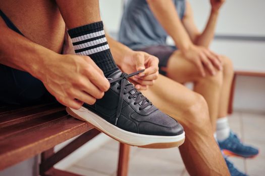 Squash player tying his shoe lace. Hands of a fit athlete getting ready for a squash match. Closeup of a player tying the laces of his sport sneaker. Player sitting on a bench with his friend.