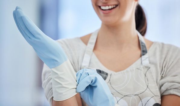 An unrecognizable domestic worker putting on rubber gloves at work. One unknown mixed race woman preparing to do housework