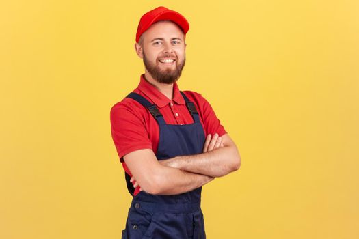 Handyman in overalls standing with crossed arms, looking at camera, profession of service industry.