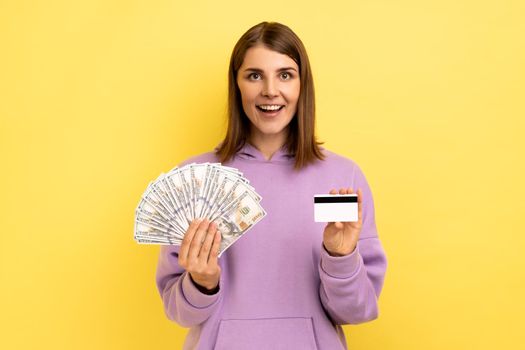 Woman with dark hair holding fan of dollars banknotes and credit card, earning money, banking.