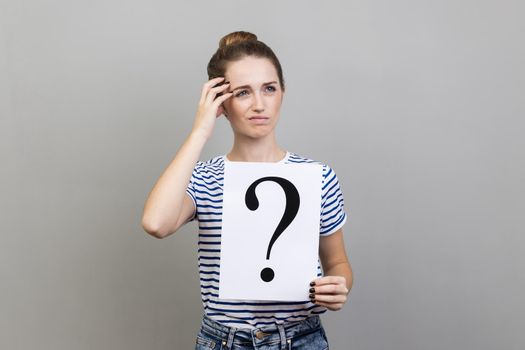 Woman looking away, holding paper with question mark, thinks about solving problem.