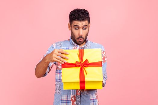 Portrait of curious happy man opening gift, peeking inside box with nosy look, unpacking present, in anticipation of interesting birthday surprise.