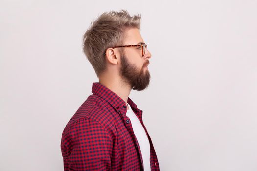 Profile portrait of confident serious bearded guy in eyeglasses and checkered shirt attentively looking right