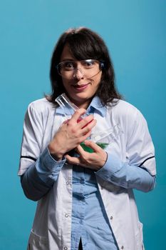 Wild looking laboratory worker holding beakers filled with unknown liquid substances while on blue background.